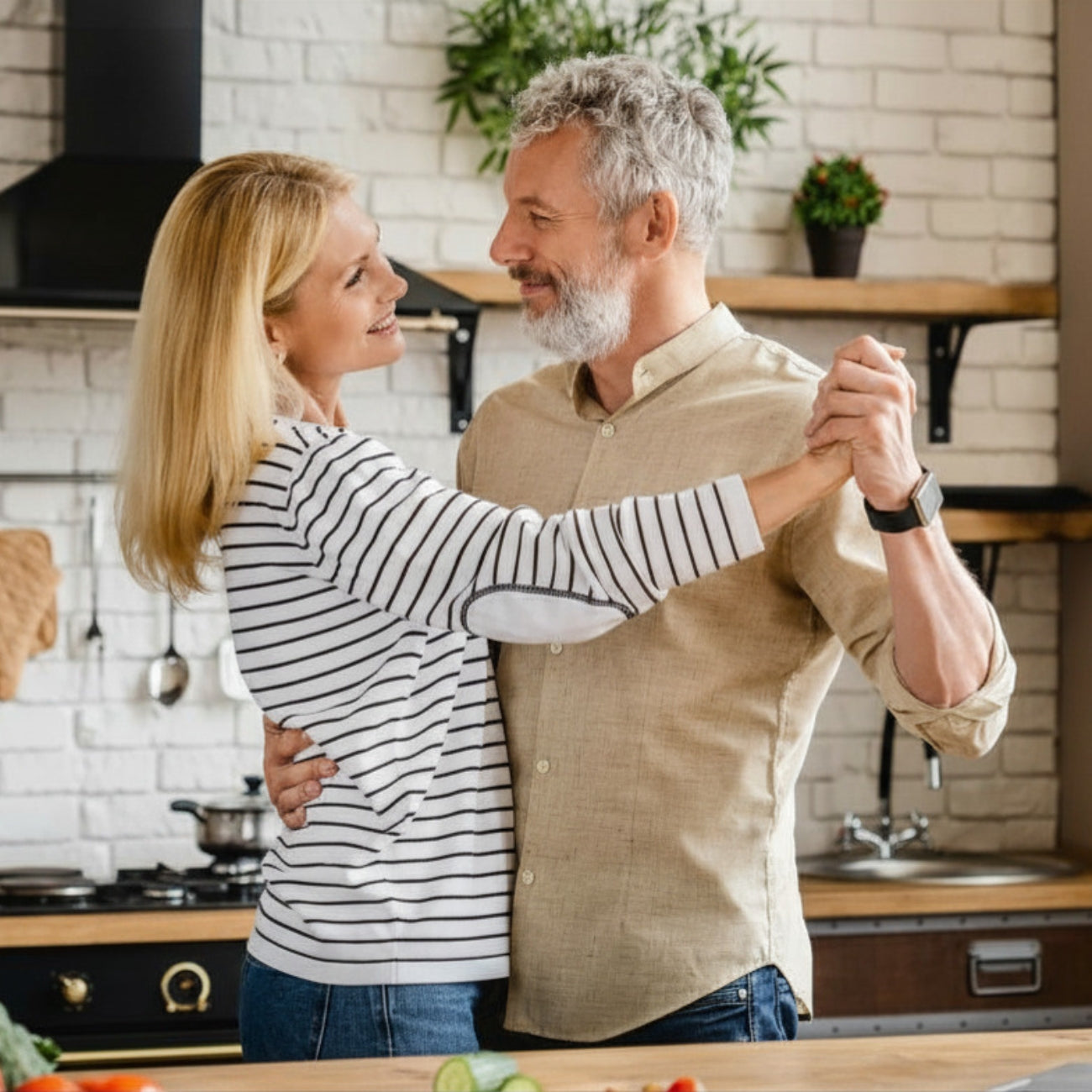 Middle aged couple dancing in a kitchen with a white brick wall background