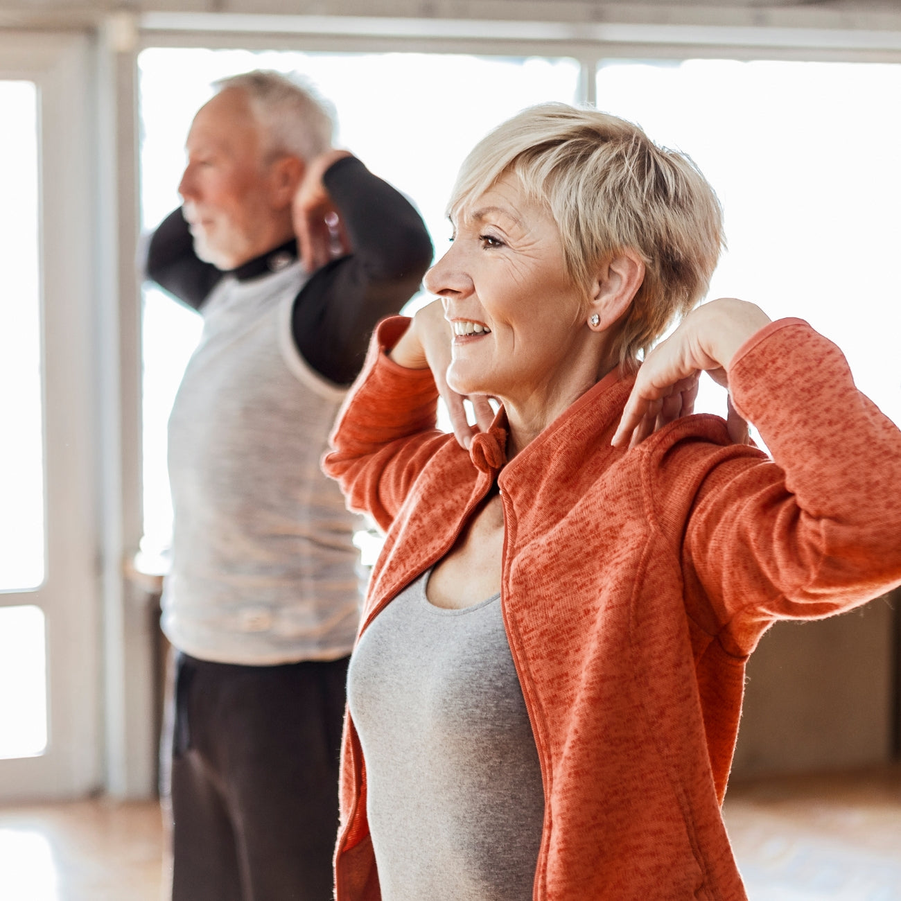 Two elderly individuals participating in a stretching exercise indoors.